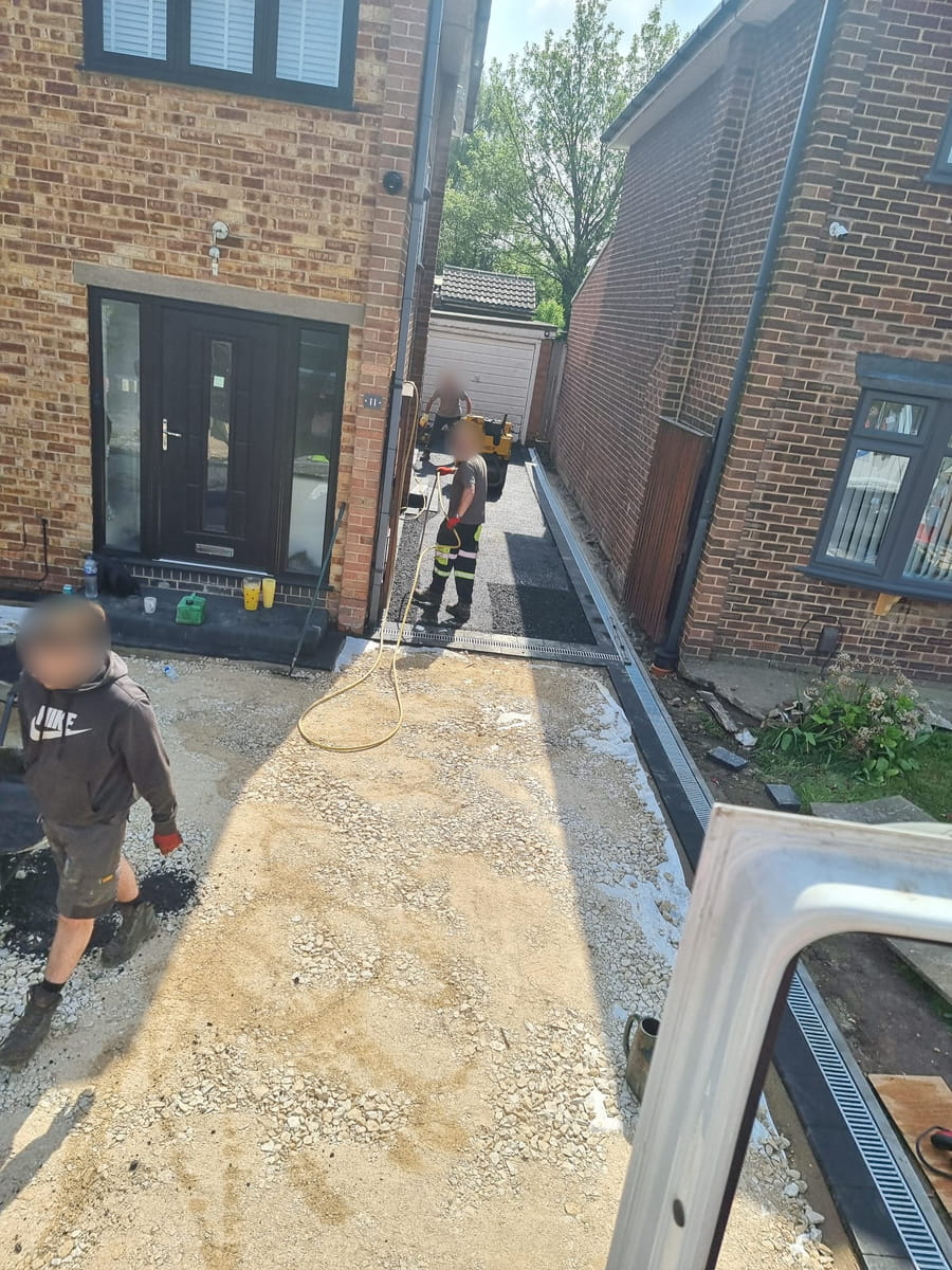 Stone base laid for a new drive, with a channel drain fitted along one side and workers on site