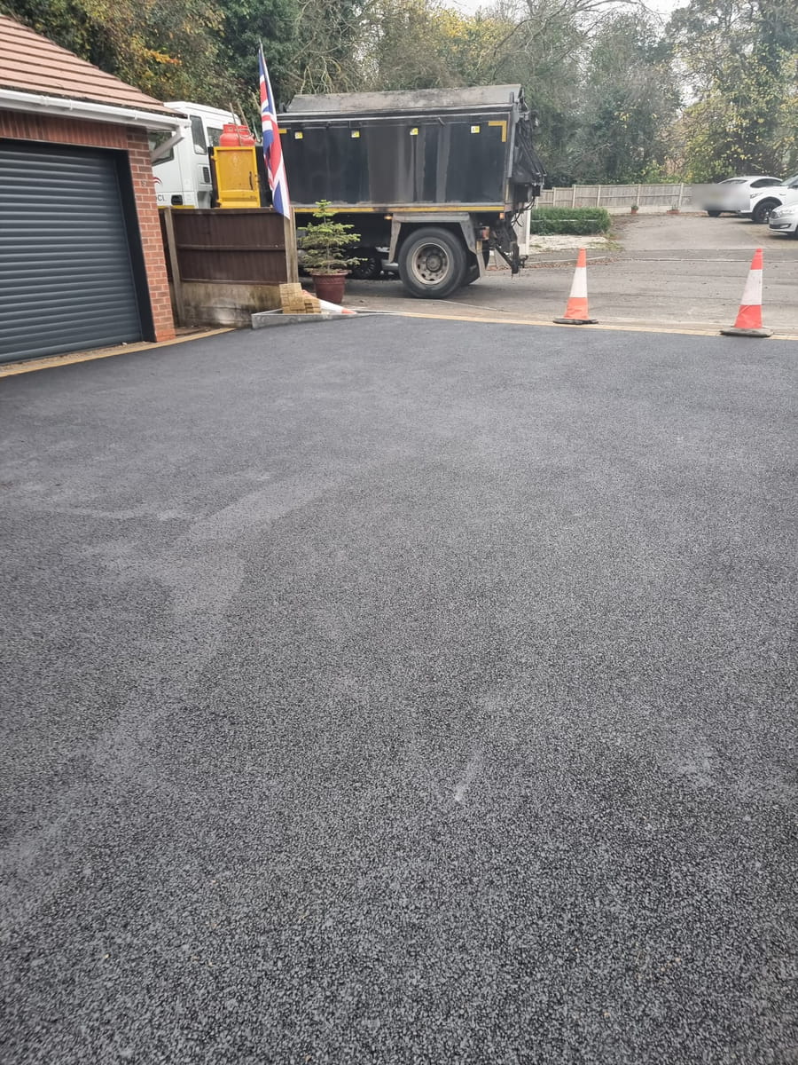 New tarmac drive beside a garage, with a lorry and traffic cones on the road behind