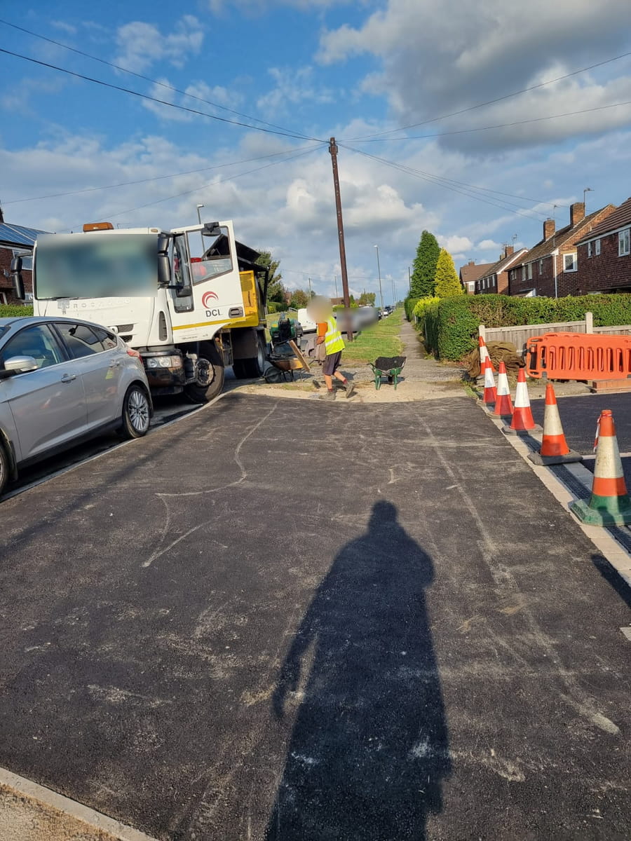 New tarmac across a footway, with a lorry at the kerb and cones along one edge