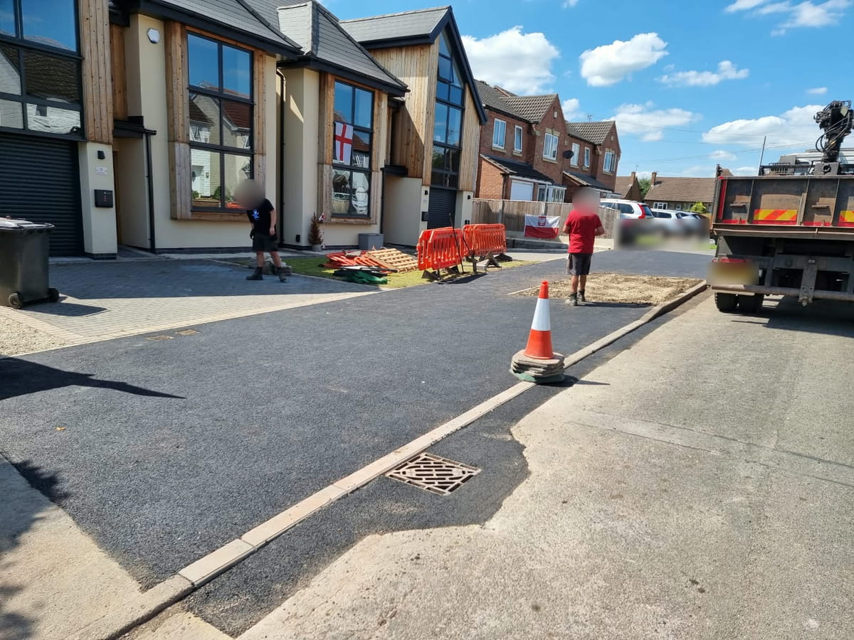 New tarmac across the pavement in front of new houses, laid up to the kerb line along the road