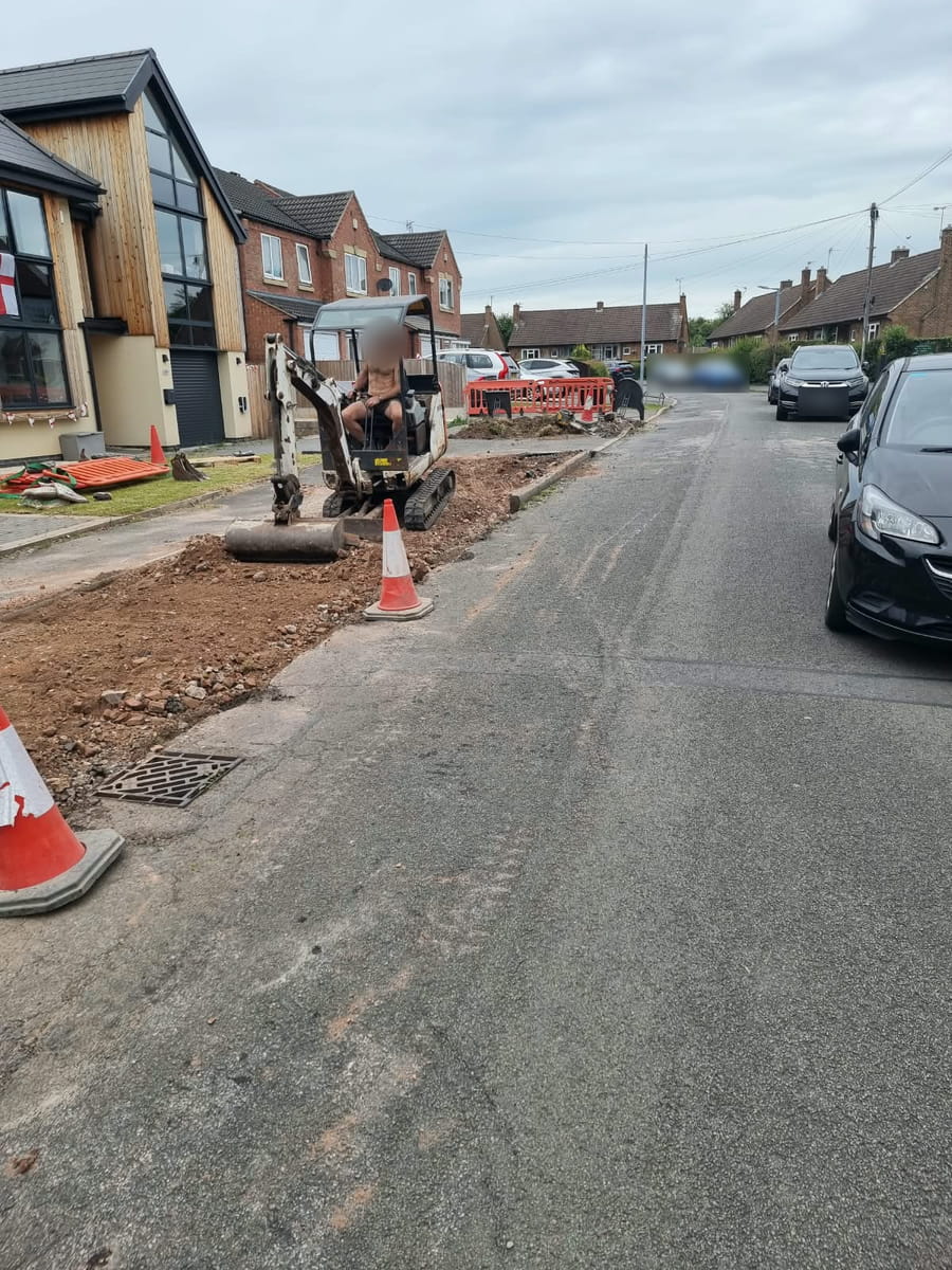Strip of pavement dug out along the road, with a mini digger and traffic cones