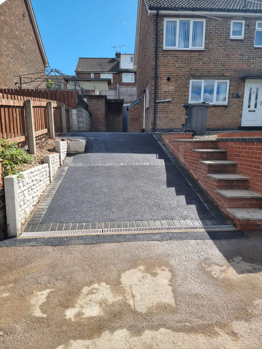 Finished tarmac driveway with block edging and a channel drain across the front, next to brick steps