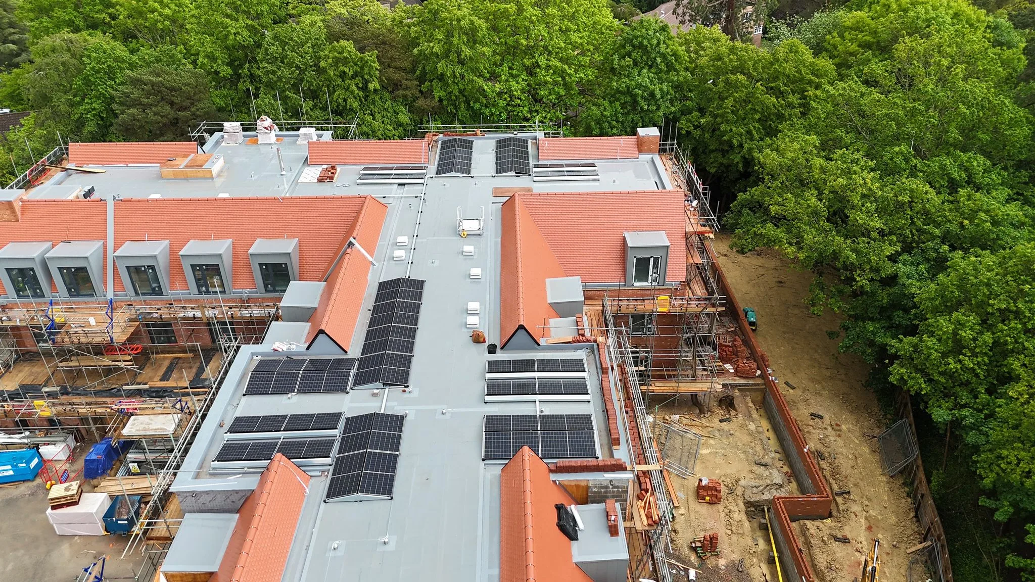 Wide aerial view of the Haywards Heath care home build showing commercial solar panel arrays mounted across the central flat-roof sections of the terracotta-tiled building, with perimeter scaffolding in place.