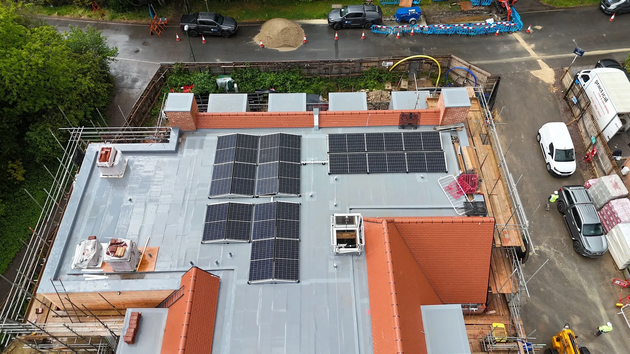 Aerial view of the commercial solar panel arrays installed on the flat roof of the Haywards Heath care home, with site parking and scaffolding around the perimeter of the building.