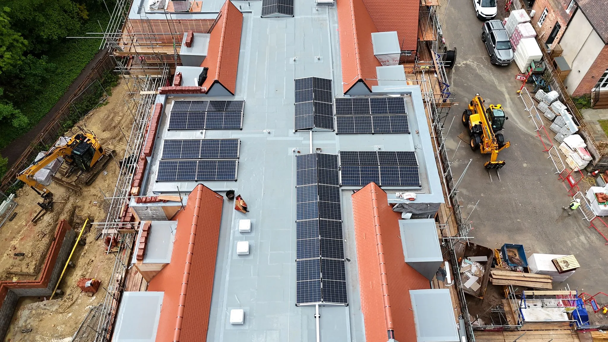 Oblique aerial of the Haywards Heath care home commercial solar installation, with telehandlers and the construction yard visible alongside the flat-roof mounted panel arrays.