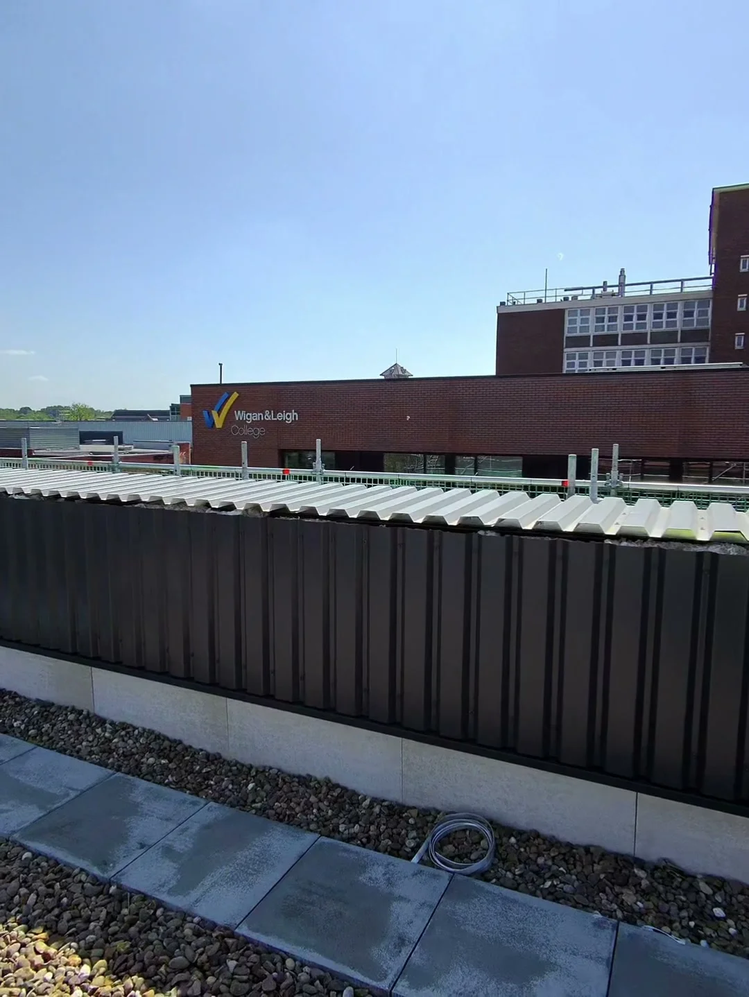 Jordan from Manchester Renewables on-site at Wigan & Leigh College, walking through the 330 kW commercial rooftop solar PV installation — Aiko panels on east-west ballasted tray across the main building flat roof.