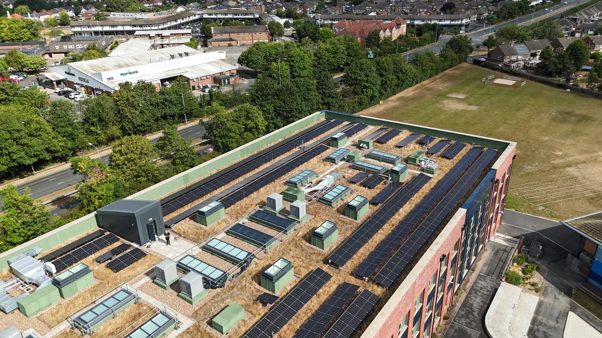 Rooftop solar array on Deyes High School, Liverpool — hundreds of panels across the flat sedum roof around skylights and plant