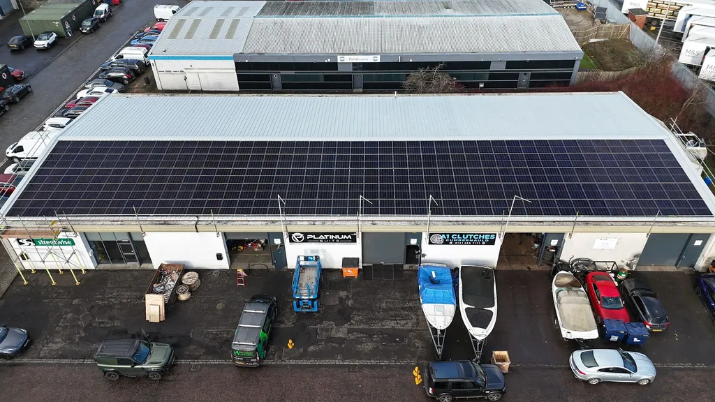 Large commercial solar array on factory building — drone shot showing full roof coverage, Manchester