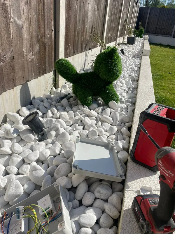 Finished garden lighting installation in a Denton pebble border — spike lights and up-and-down lights wired to a Quinetic wireless switch system