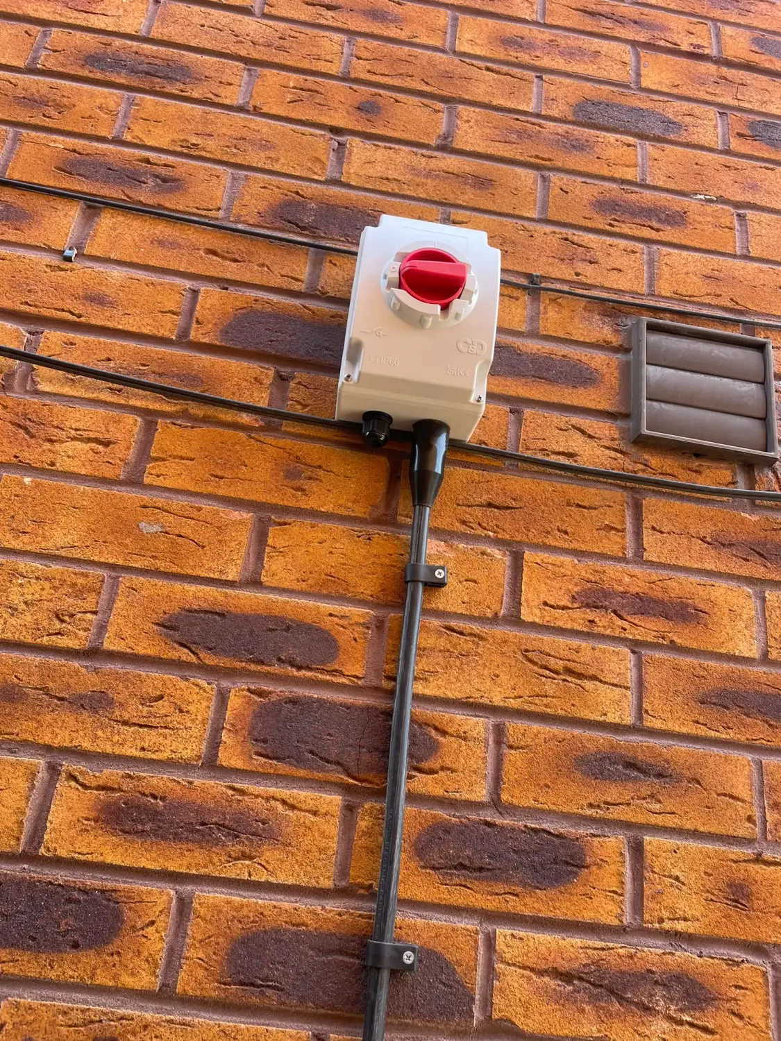 Weatherproof 40A rotary isolator installed on an external brick wall in Glossop, fed in SWA cable, ready for a new air conditioning unit — by Steels Electrical
