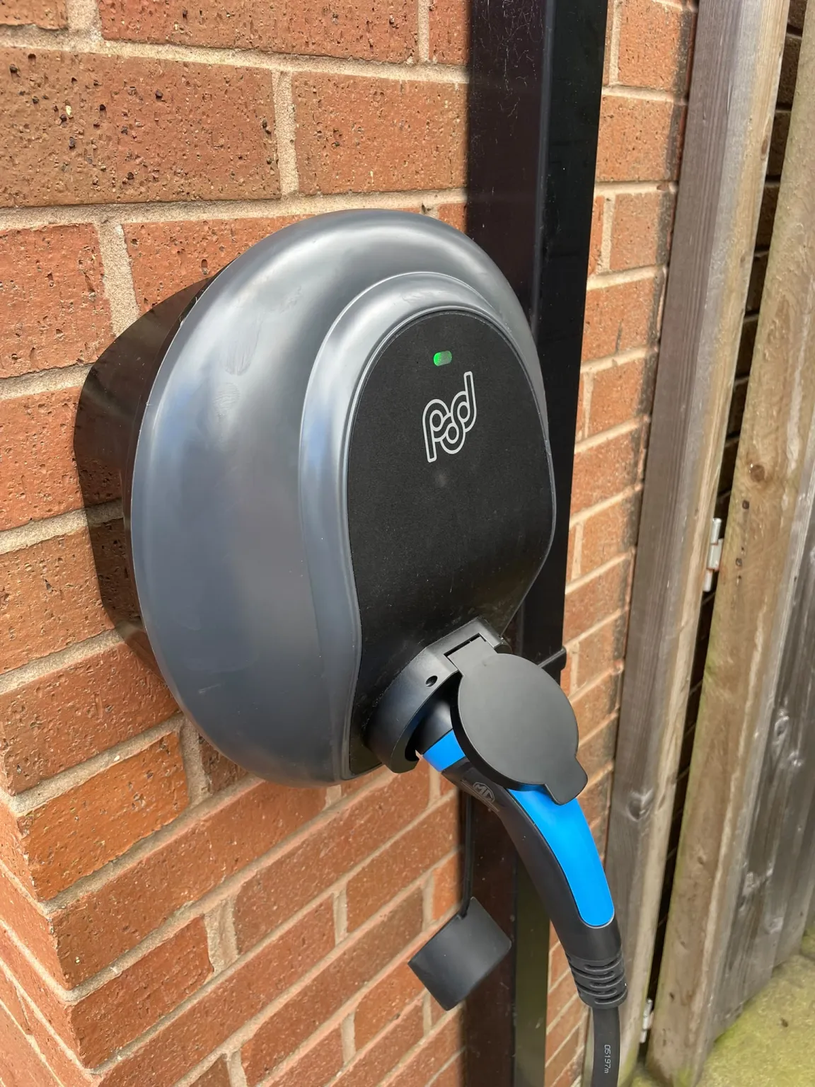 Pod Point Solo 3 7kW EV charger installed on a brick house wall in Marple, tethered Type 2 lead attached and status light on — Steels Electrical